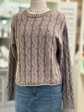 Brown cable knit sweater on a mannequin with a blurred indoor background