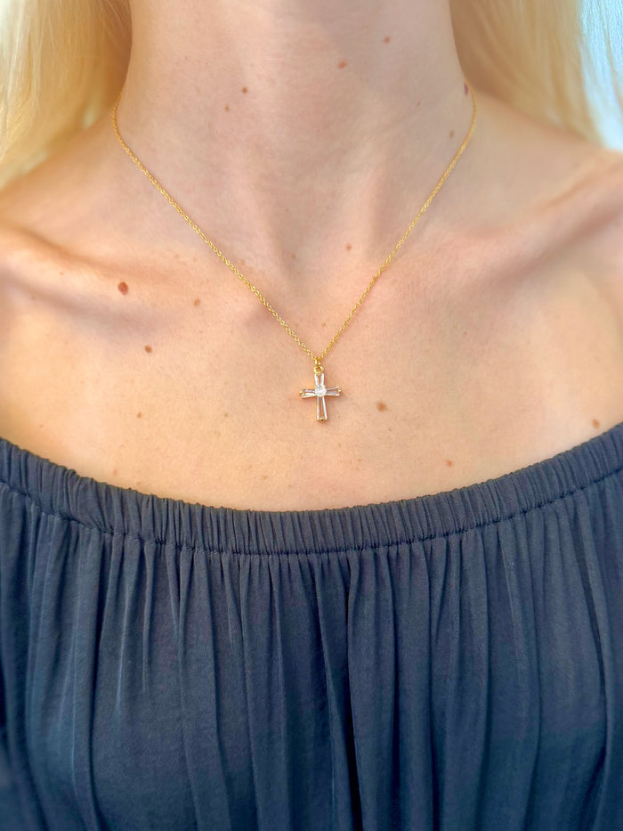 Gold necklace with a cross pendant worn by a person in a black top.