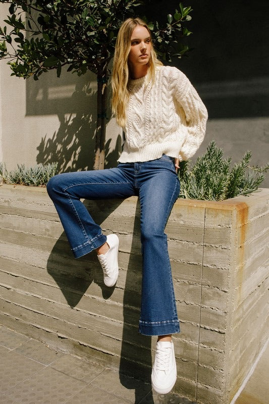 Model wearing high-rise bootcut jeans and white cable knit sweater.