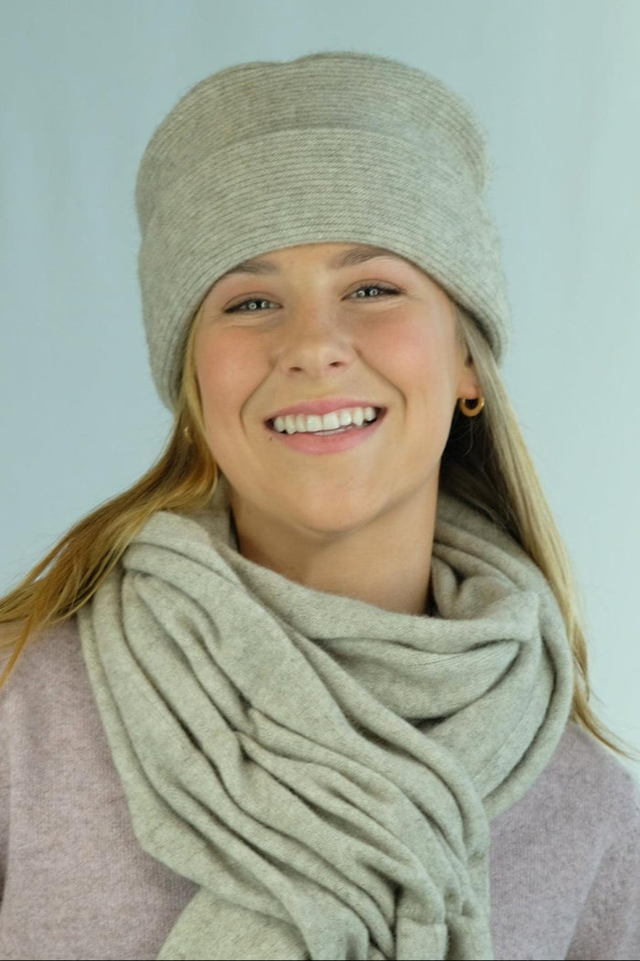 Woman wearing a beige knit hat and scarf against a light blue background