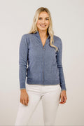 Woman wearing a blue zip-up sweater and white pants on a plain background