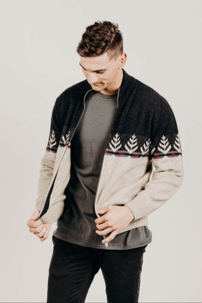 Man wearing a black and beige patterned sweater over a gray shirt on a plain background