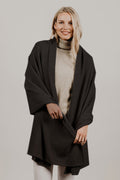 A woman smiling, wearing a black Merinosilk travel wrap draped over her shoulders.