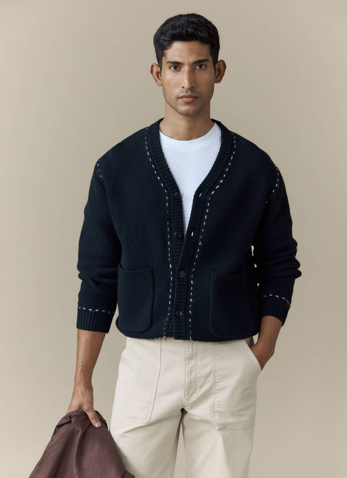 A model wears the black Module Boxy Cardigan from Percival, styled with a white t-shirt and cream trousers.