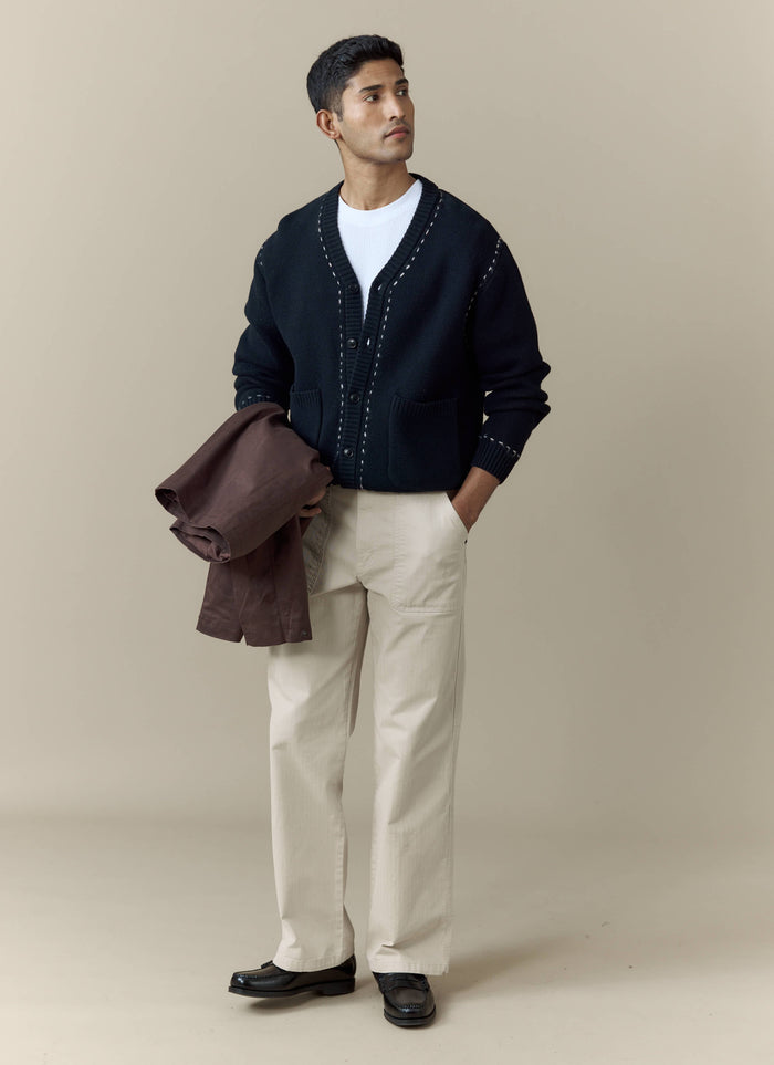 A model wears the black Module Boxy Cardigan from Percival, styled with beige trousers and a white t-shirt.