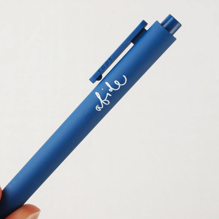 Blue pen with 'abide' in cursive text held by a hand on a light gray background