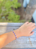 Hand wearing a blue and silver bracelet on a wooden surface with a blurred natural background