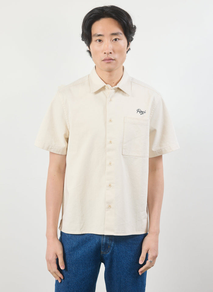 A model wears the Percival Olive Embroidered Cropped Shirt in off-white, showing the front view with Perci chest embroidery.