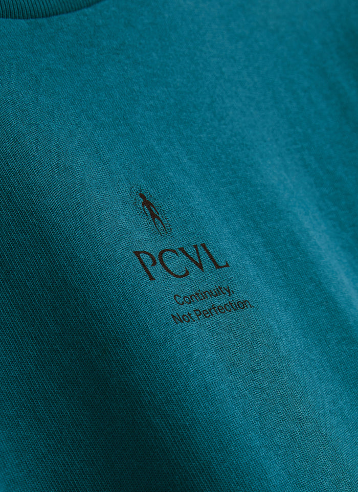 A close-up of the 'Continuity, Not Perfection' PCVL chest print on the blue Aura Boxy T-shirt by Percival.