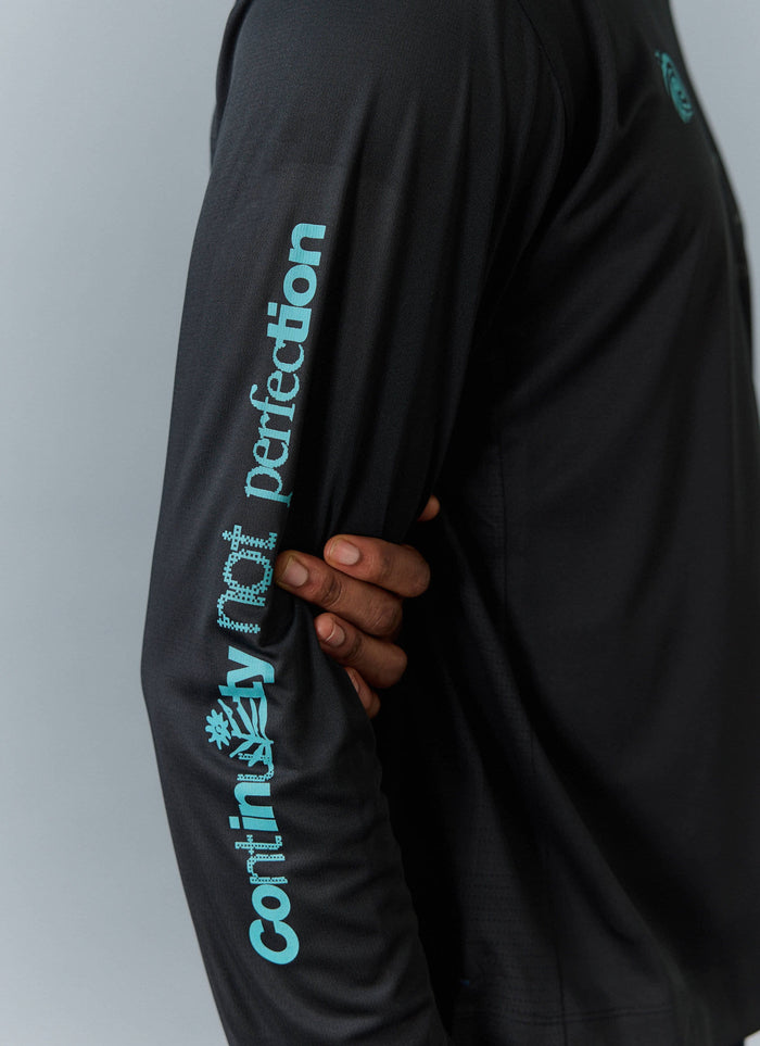 Close-up of the black PCVL Performance Top from Percival, showing the blue 'Continuity not perfection' graphic on the sleeve.