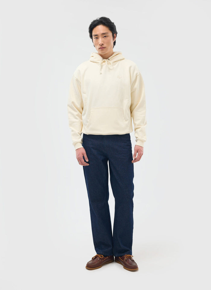 A model wears the ecru Perci Chainstitch Hoodie by Percival, styled with dark wash jeans and brown boat shoes.