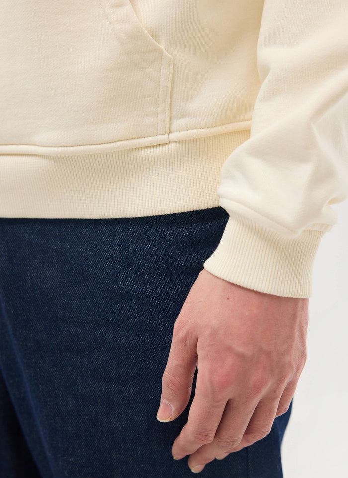 A close-up of a model wearing the Percival Perci Chainstitch Hoodie in ecru, showing the ribbed cuff and hem detail.