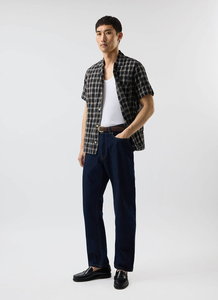 A model wears the Percival Ryco Cuban Collar Shirt in a black and white check, styled over a white vest with dark jeans.