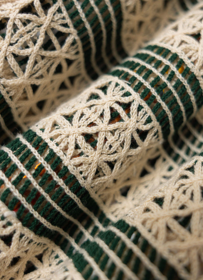 A close-up of the intricate crochet-style knit on the Percival Sarti Knitted Polo Shirt in ecru and forest green.