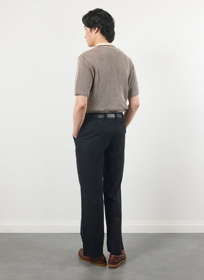 A male model seen from the back wearing the Percival Teramo Knitted Polo in ecru, paired with smart black trousers.