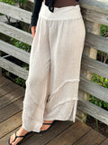 Light beige wide-leg linen pants with frayed seam details and a soft fold-over waistband, styled with a black top and sandals.