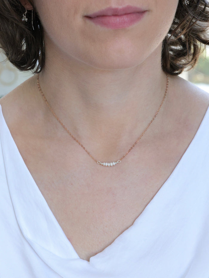 Woman wearing a delicate rose gold chain necklace with five small white pearls centered on it, styled with a white blouse for a minimalist, elegant look.