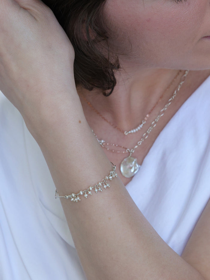 Woman wearing layered pearl necklaces and a delicate silver bracelet adorned with small pearl drops from Ardor Boutique, styled with a soft white top for an elegant, feminine look.