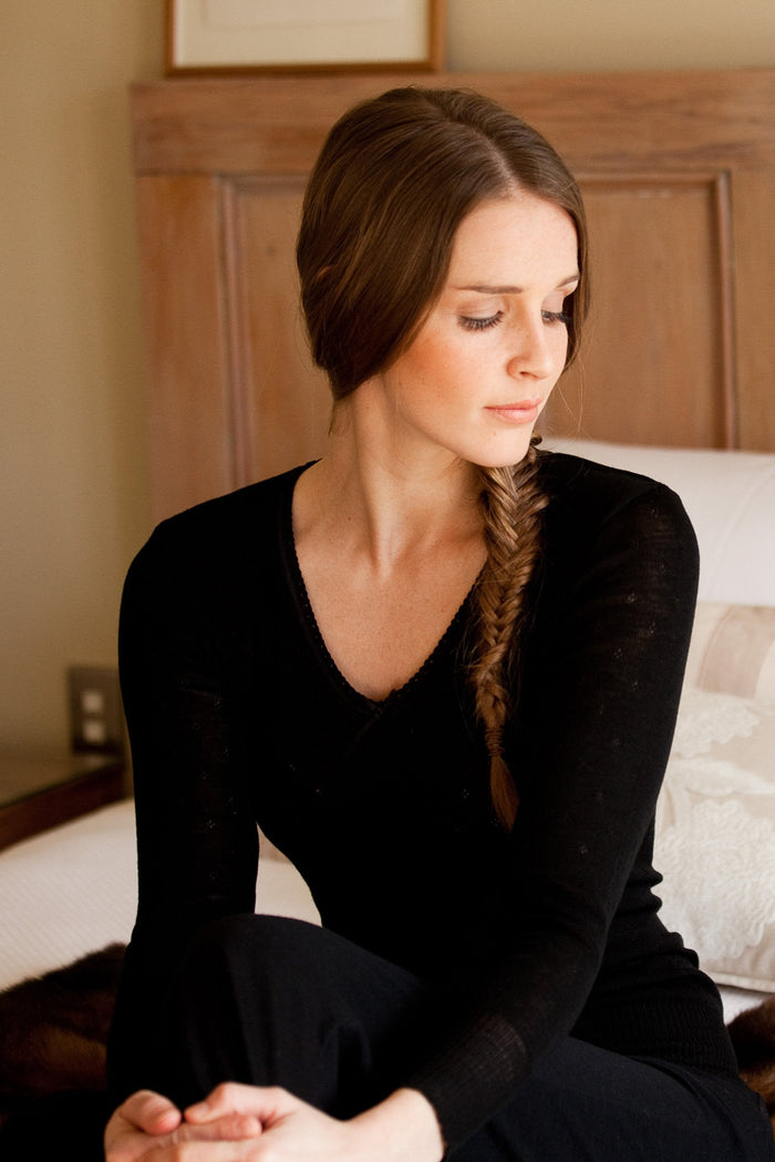 A woman sitting and wearing a long sleeve black merino thermal top with a V-neck.